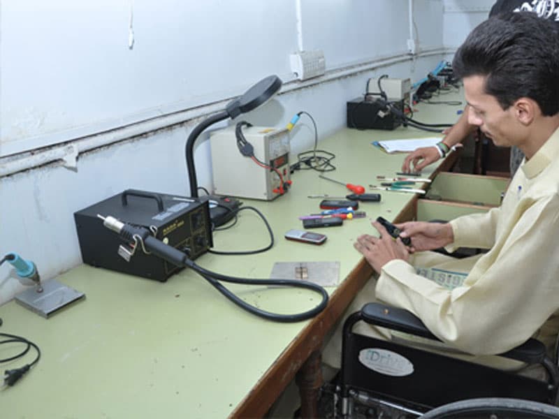 Person using a wheelchair repairing a mobile phone at the Skill Development Centre