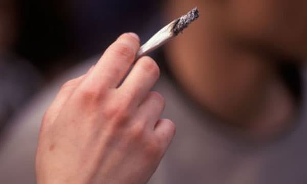 Close-up of a hand holding a lit cigarette, representing substance abuse